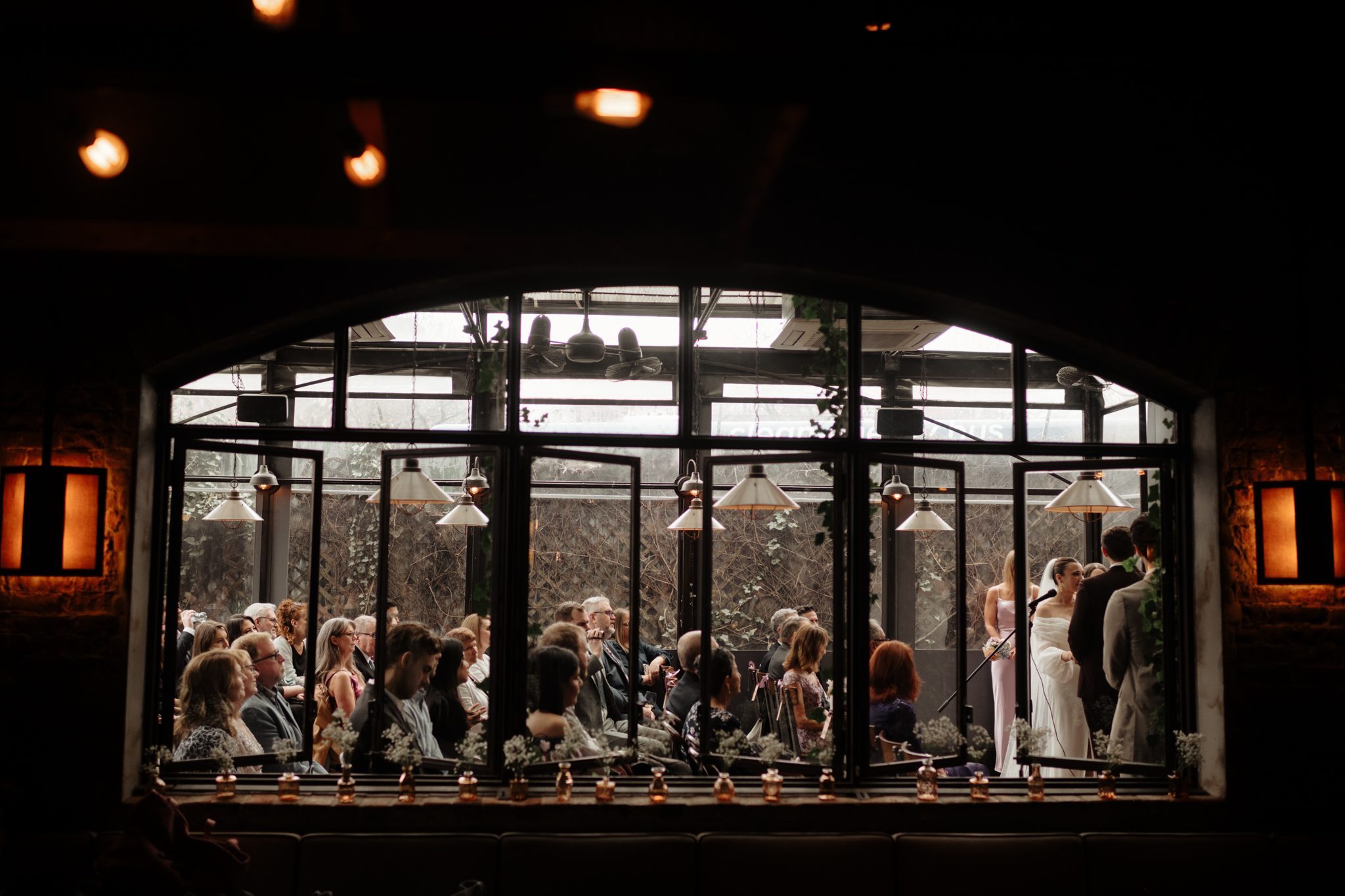 Wedding ceremony at Aurora Brooklyn seen through the arched restaurant windows | New York wedding photographer Tonie Christine